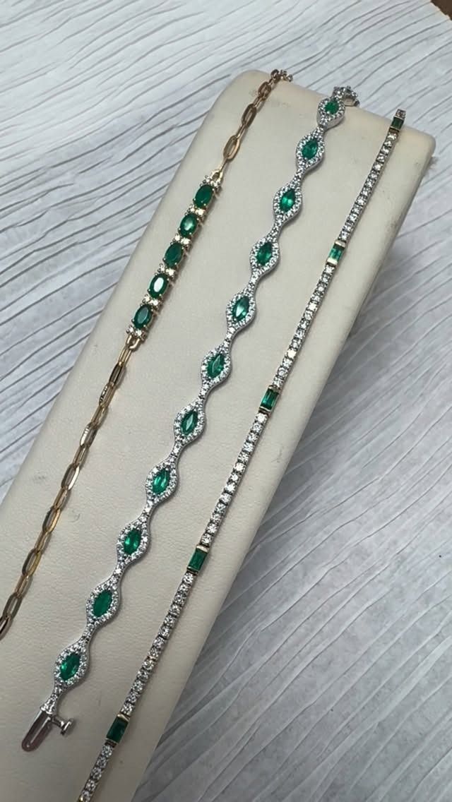 Three emerald and diamond bracelets displayed on a white surface.