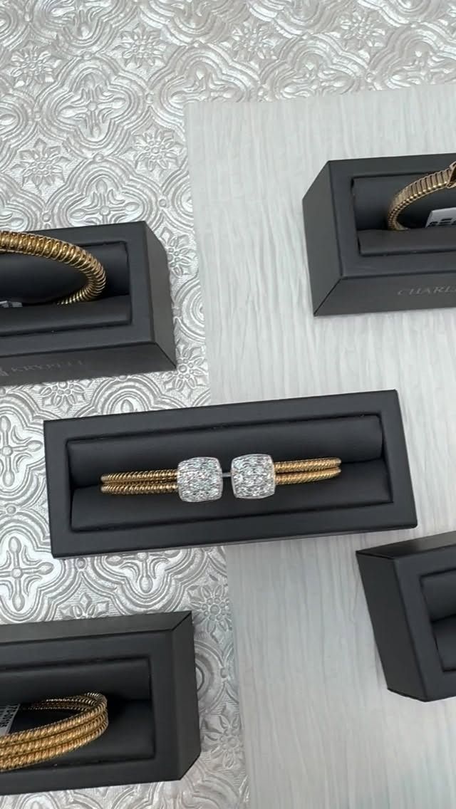 Gold bracelets displayed on black stands, set against a patterned white backdrop.