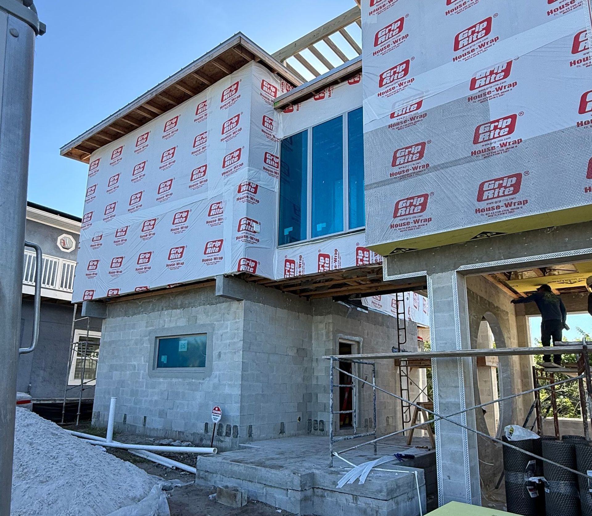 House under construction, unfinished concrete structure, scaffolding, sunny outdoor setting.