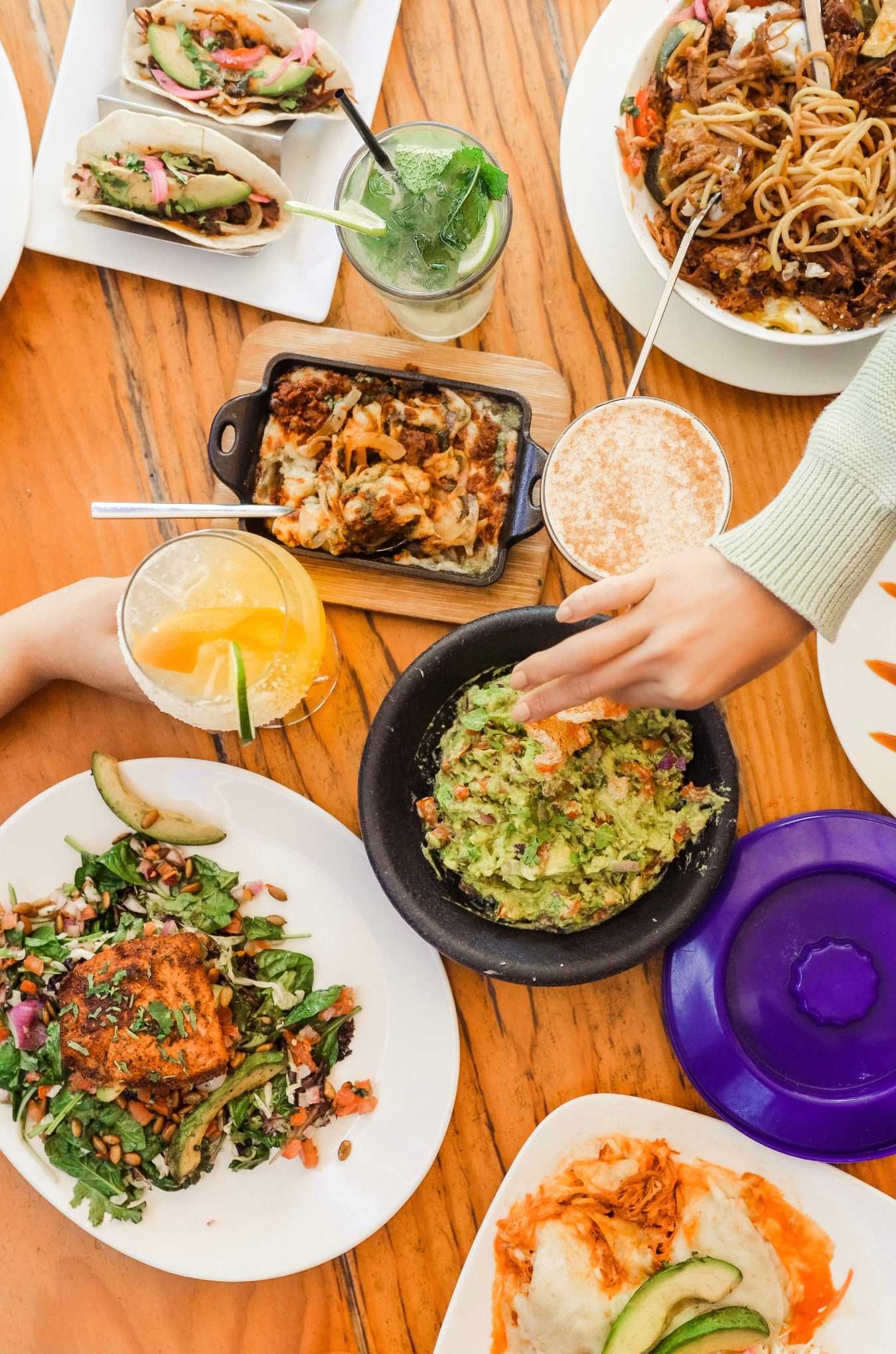 Person using fork to eat breakfast bowl with egg, tacos, and drink in the background.