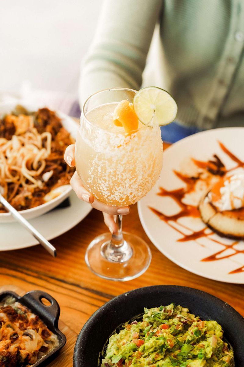 Person eating a dish with an egg on a rectangular plate, next to a cocktail.