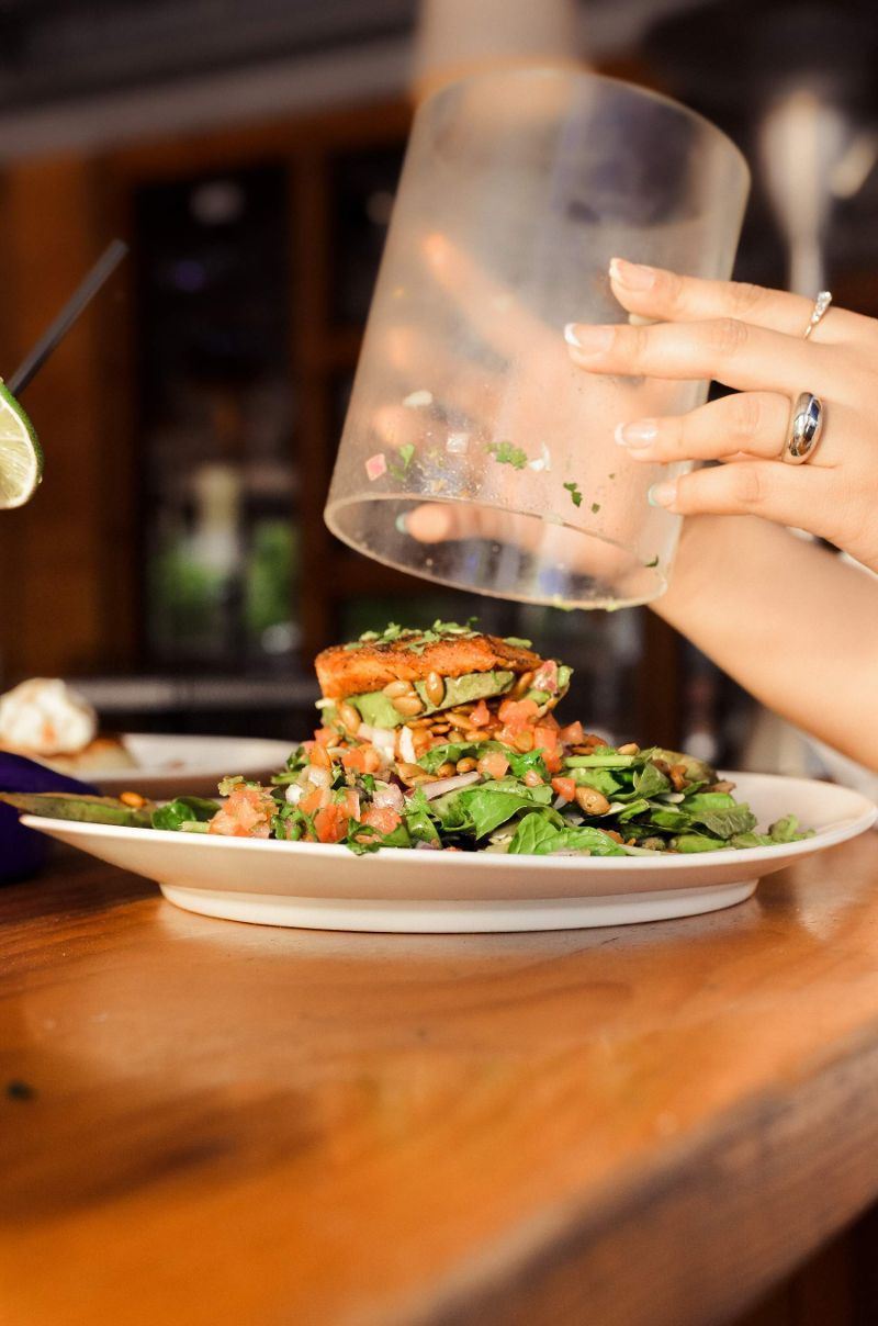 Chef pouring sauce over a bowl of food with an egg. Outdoor restaurant setting.