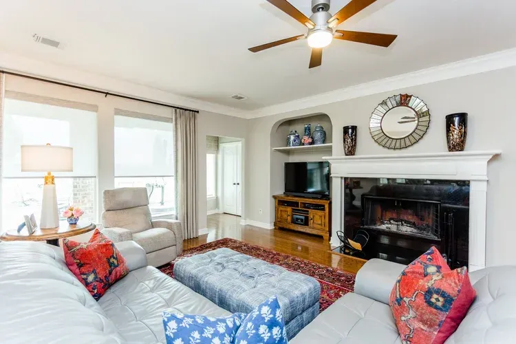 Bright living room with gray sofas, red accents, fireplace, TV, and ceiling fan