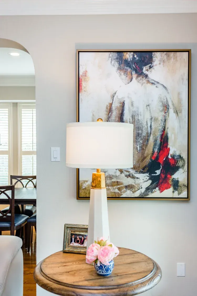 Modern console table with lamp and flowers beneath abstract painting in a light beige room