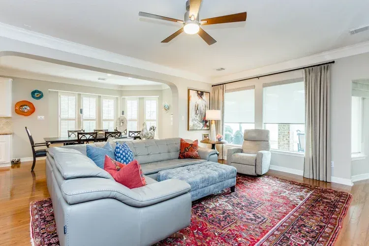 Bright living room with a gray sectional, red rug, ceiling fan, and large windows