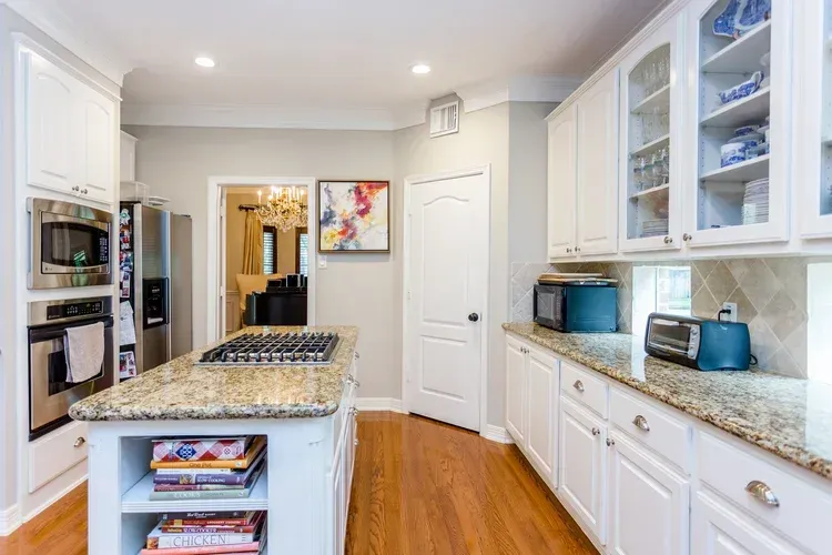 Bright kitchen with white cabinets, granite island, wood floors, and a framed wall art piece.