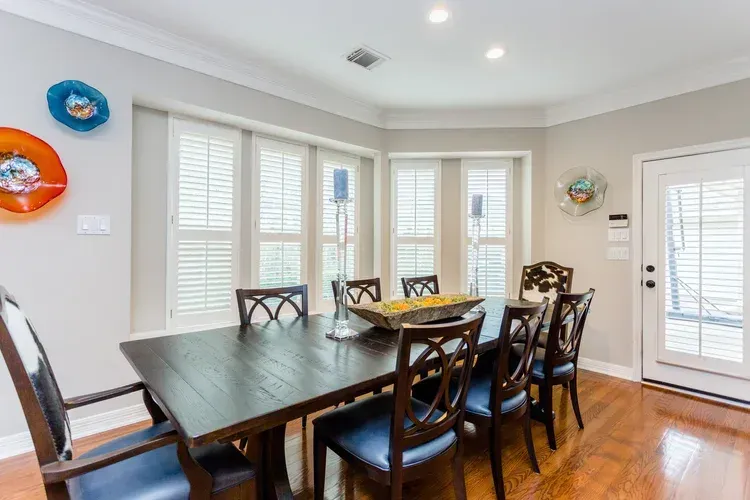 Bright dining room with dark wood table, chairs, white shutters, and hardwood floors