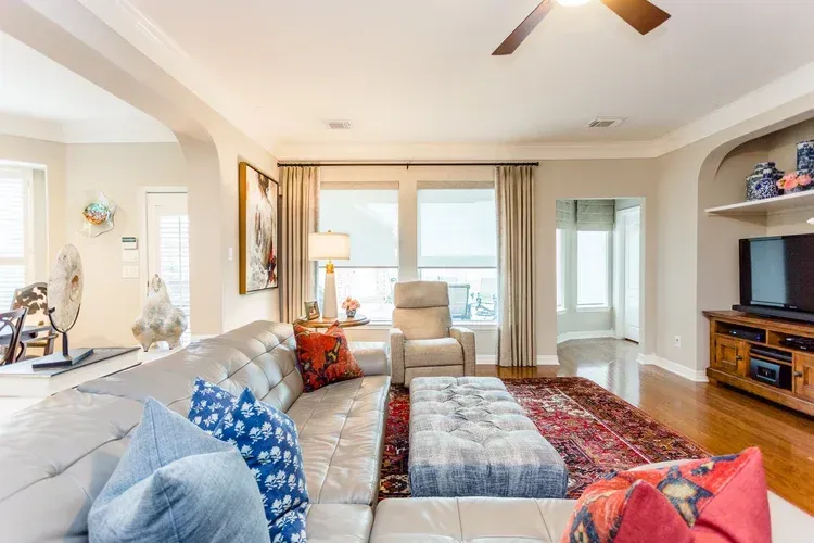 Bright modern living room with beige sectional, colorful pillows, red rug, and balcony doors.