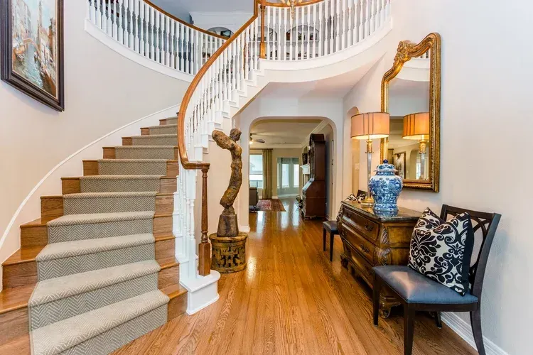 Elegant foyer with curved staircase, hardwood floors, and a console table with mirror and lamp