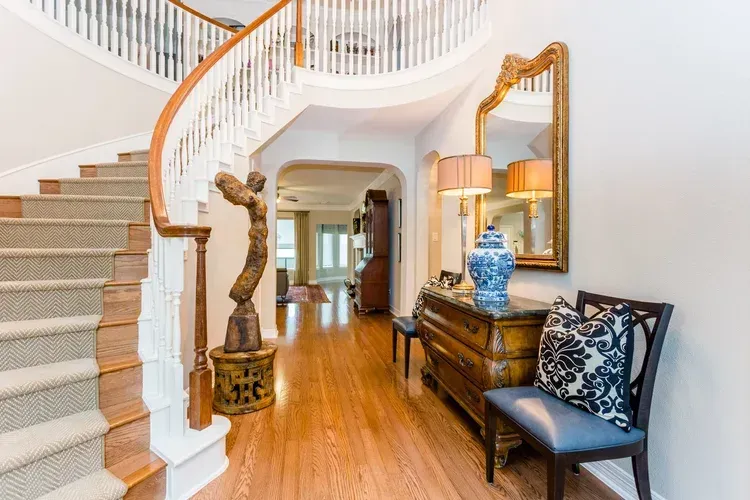 Elegant foyer with a curved staircase, hardwood floors, console table, mirror, and upholstered chair.