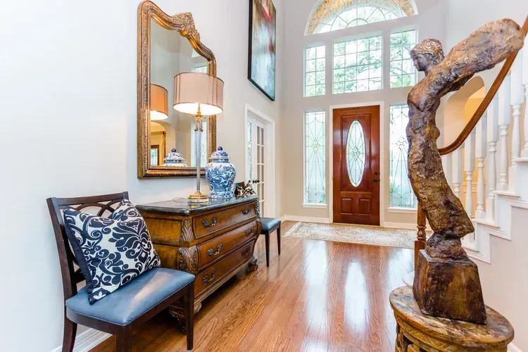 Bright entryway with wooden floor, console table, mirror, lamp, and a sculptural tree trunk stand.