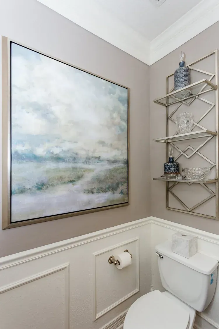 Small bathroom with a toilet, wall art, and a corner metal shelf over a taupe wainscoted wall