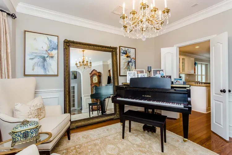 Elegant living room with a black grand piano, large mirror, chandelier, and cream armchair