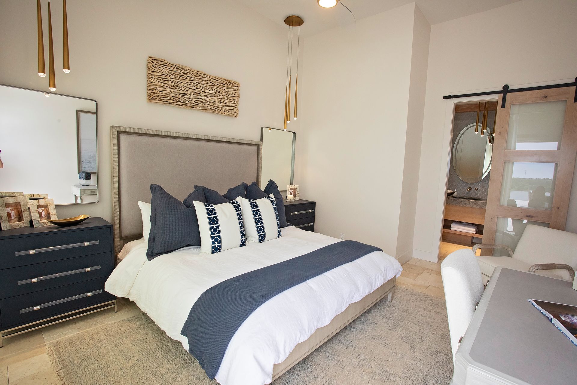 Bright modern bedroom with a gray bed, navy and white bedding, dresser, mirror, and desk by the window