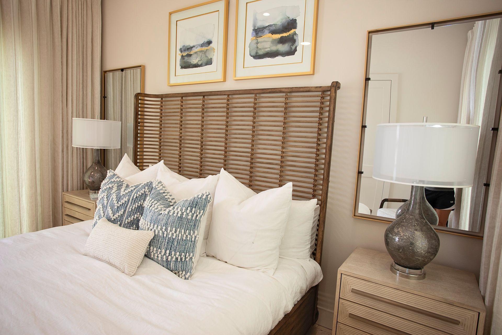 Cozy bedroom with a wicker headboard, white bedding, framed art, and a mirror above a nightstand.