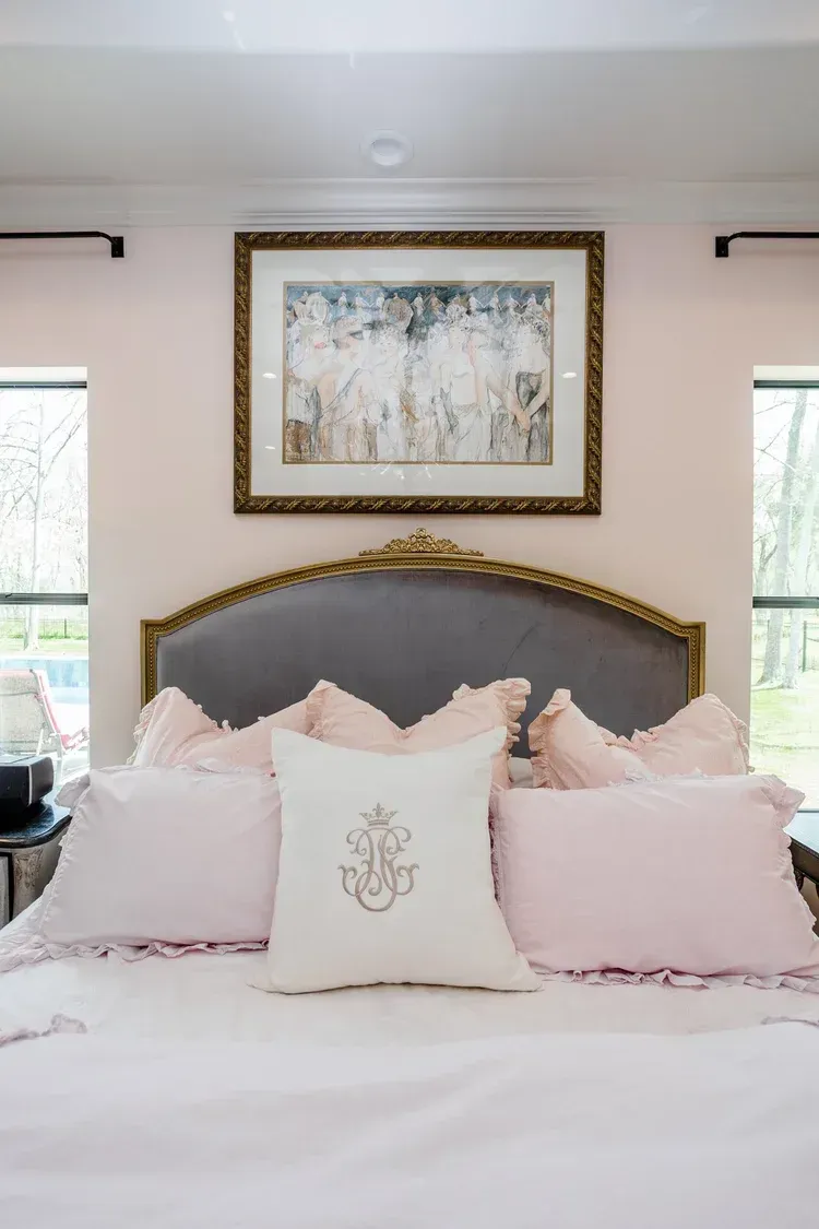 Elegant bedroom with a tufted gray headboard, blush bedding, and framed artwork above the bed