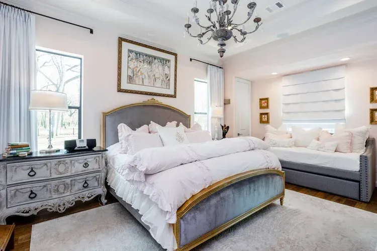 Elegant bedroom with tufted bed, gray chaise, vintage dresser, chandelier, and bright white decor
