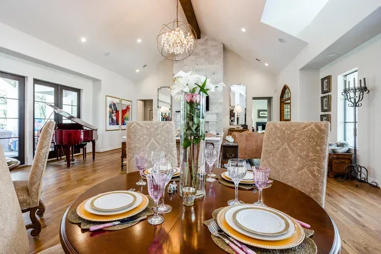 Elegant dining room with set table, chandelier, white walls, and piano near tall windows