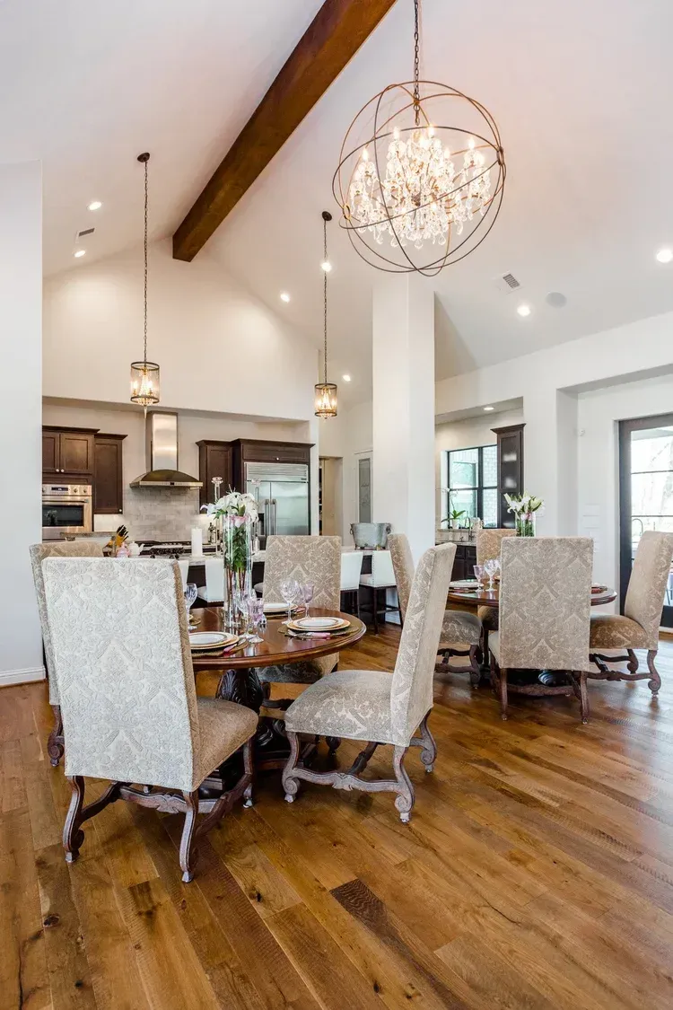 Spacious dining room with high ceilings, chandelier, wood floors, and a round table with upholstered chairs.