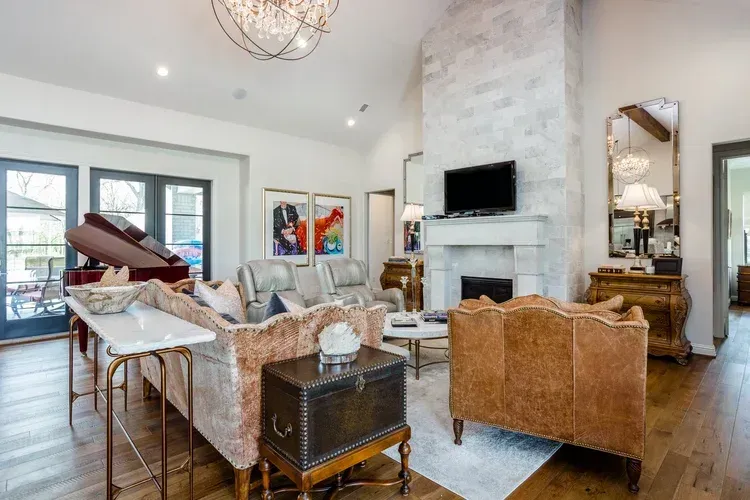 Bright living room with wicker chairs, piano, white fireplace, and large windows