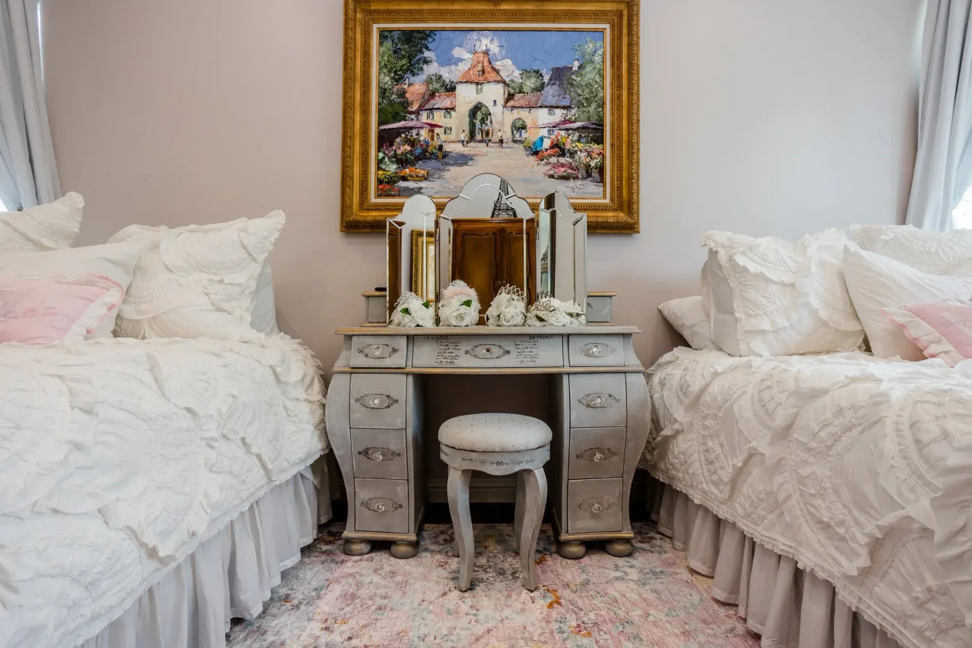 Elegant bedroom with two white beds, ornate vanity, and colorful framed painting above it