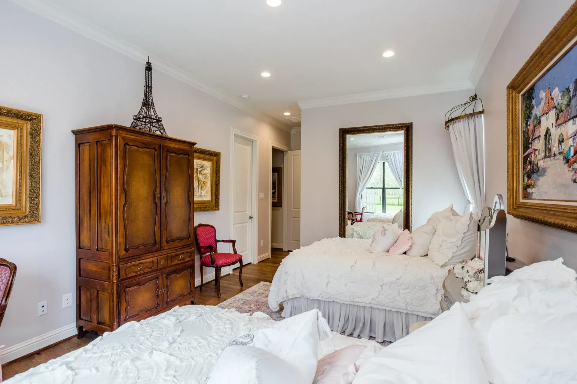Elegant bedroom with a large bed, wooden armoire, red chair, and French doors to a balcony.