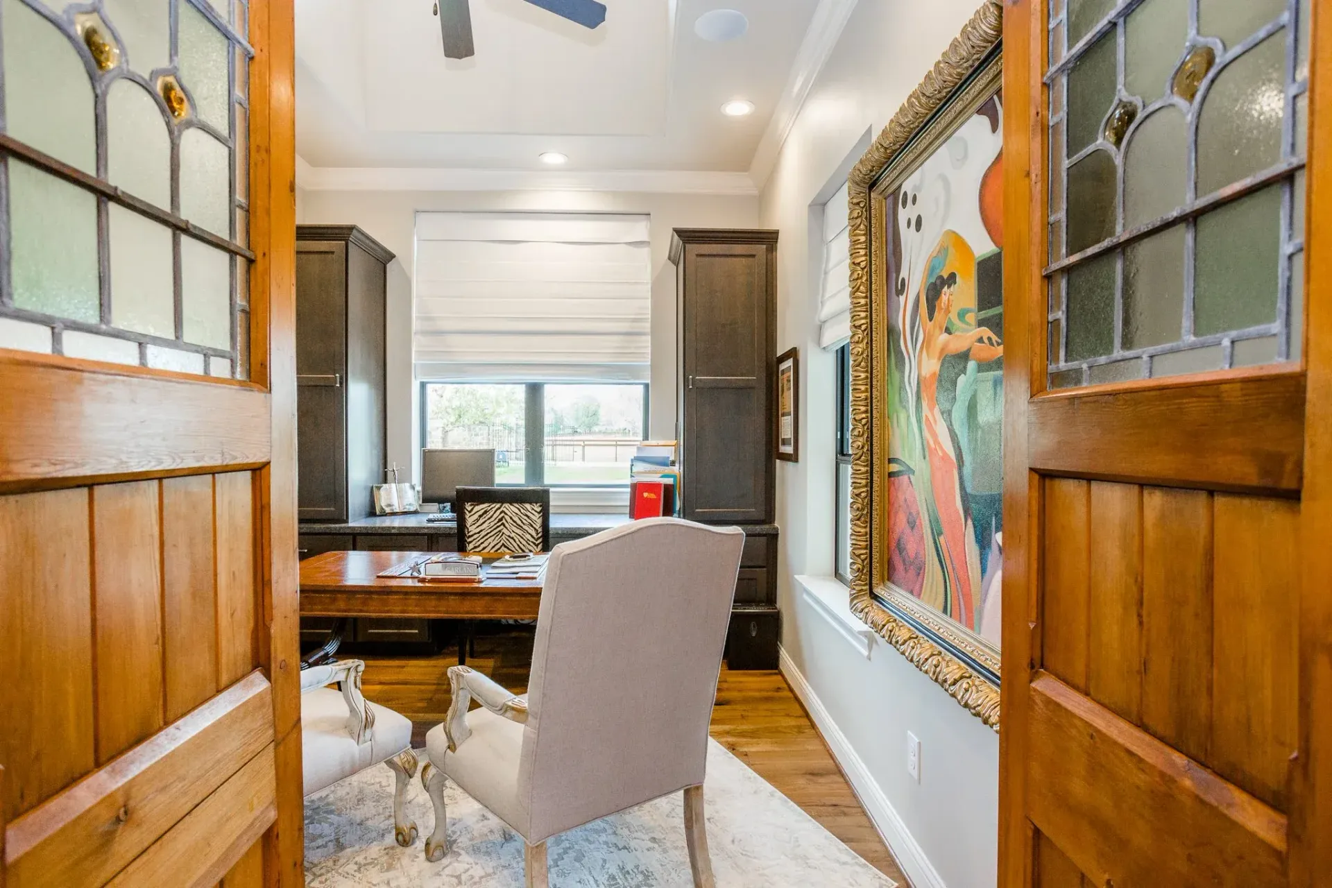 Bright hallway with wooden doors, a chair, desk, and a large colorful artwork on the right wall.