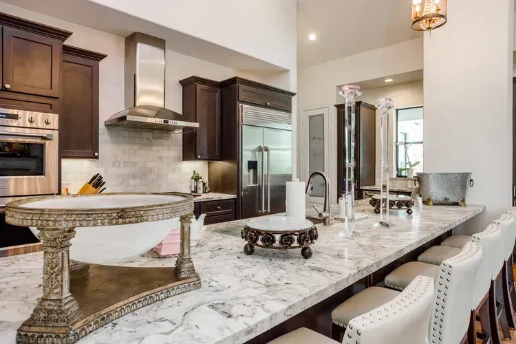 Modern kitchen with marble island, dark wood cabinets, stainless steel appliances, and bar stools