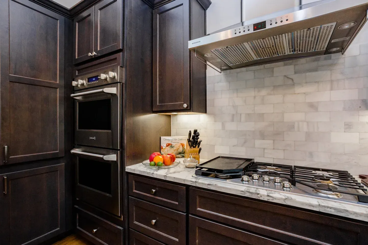 Dark kitchen with built-in oven, gas cooktop, marble backsplash, and fruit on the counter