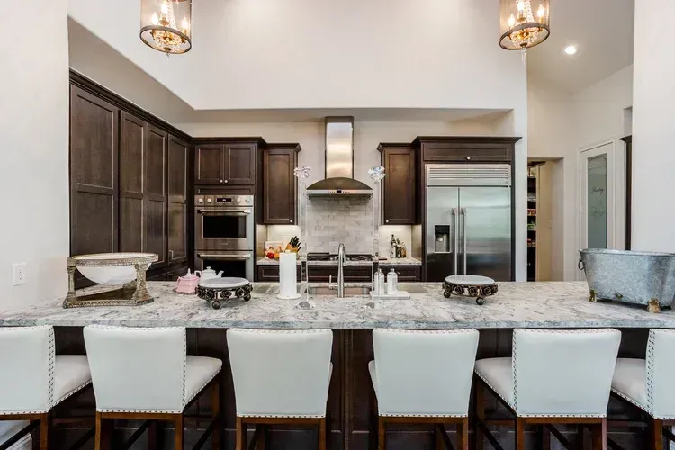 Modern kitchen with a large granite island, dark wood cabinets, and white bar stools