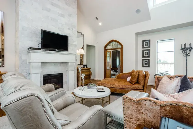 Bright living room with white fireplace, wall-mounted TV, wicker and gray seating, and arched doorway