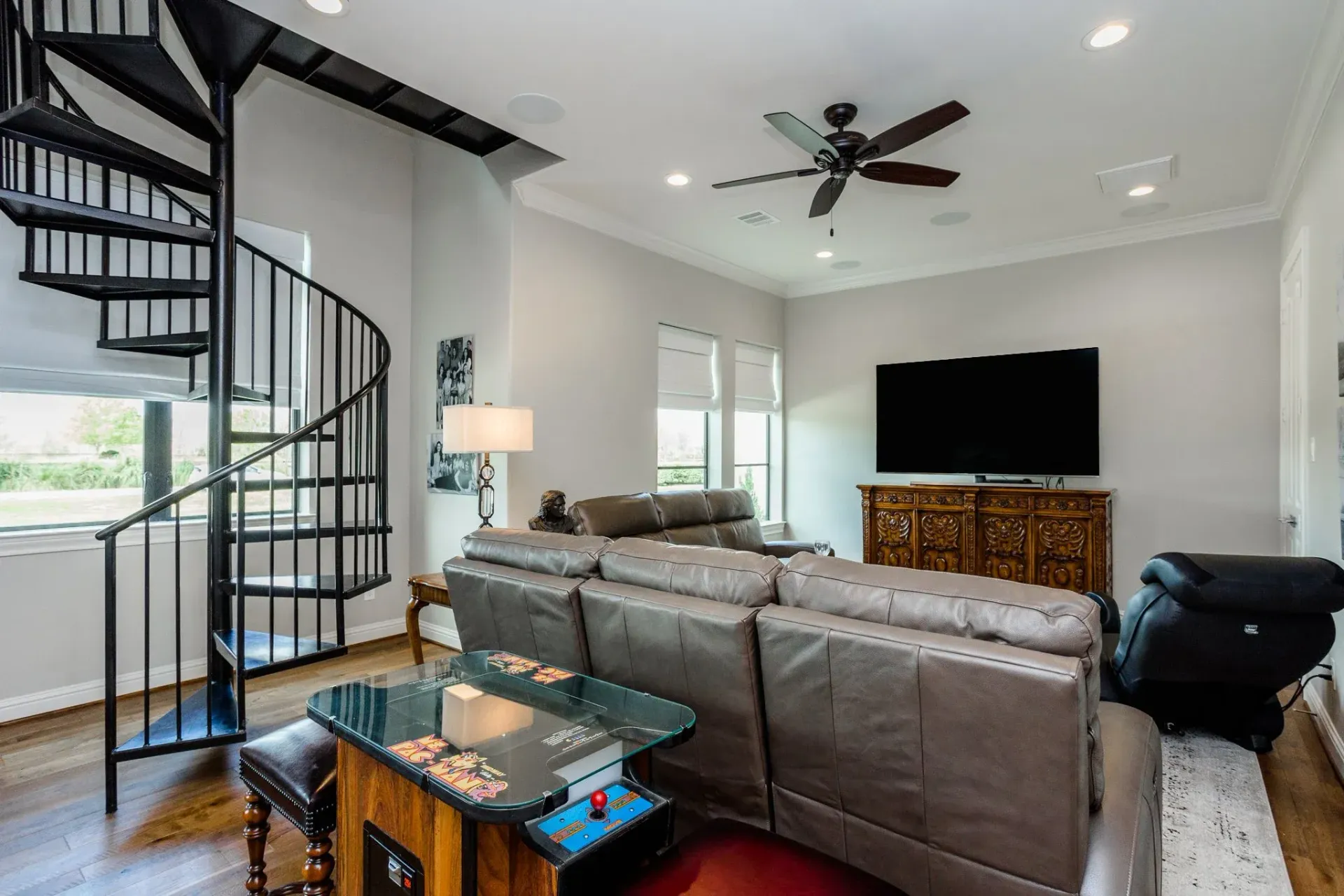 Modern living room with spiral staircase, gray sectional sofa, TV, and glass coffee table