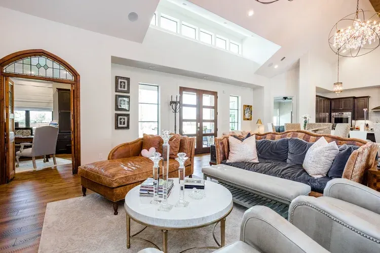 Bright modern living room with gray sofas, tan leather ottoman, round coffee table, and arched doorway to dining area