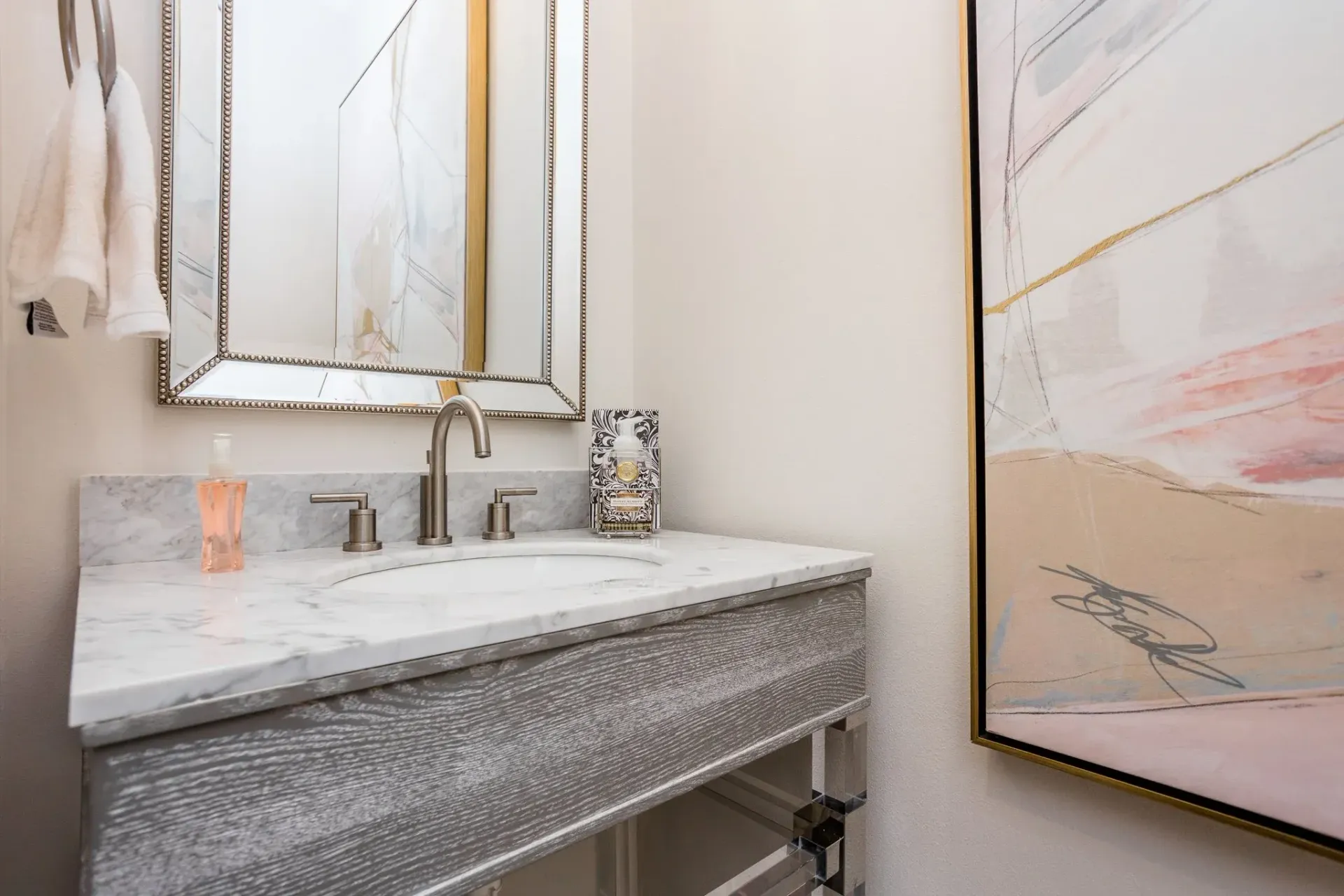 Small bathroom vanity with marble sink, ornate mirror, and framed wall art