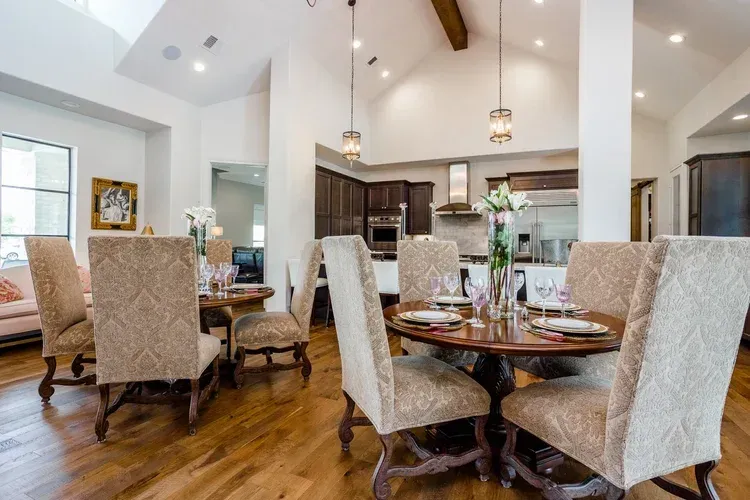 Bright open dining room with round table, upholstered chairs, wood floors, and pendant lights