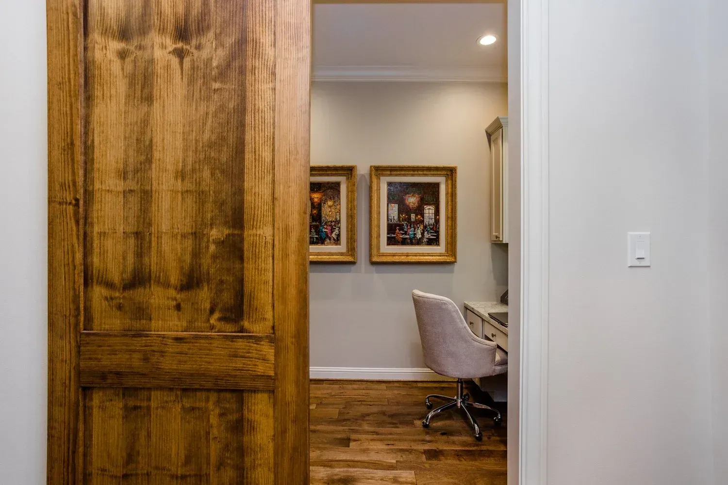 Wooden sliding door opening to a modern room with framed art, a chair, and hardwood floors.
