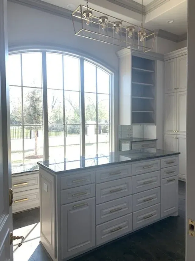 Bright white kitchen island with gray cabinetry beneath a large arched window in a sunlit room