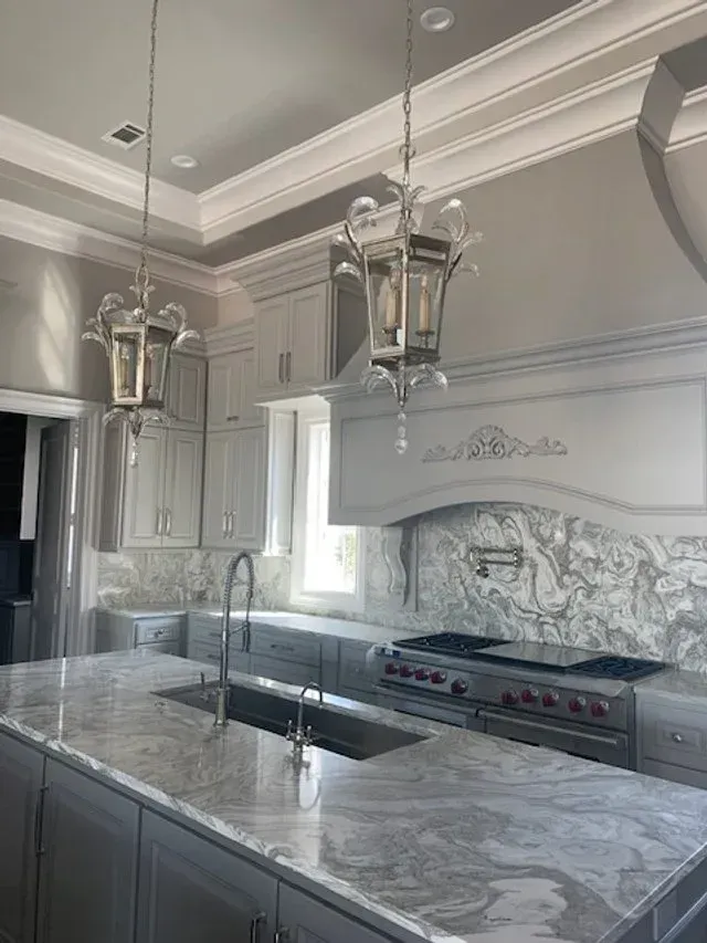 Bright gray kitchen with marble island, stainless sink, stove, and hanging lantern pendant lights.