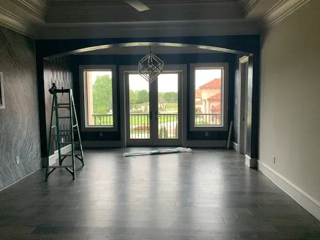 Empty modern room with dark floors, arched windows, and a ladder on the left wall.