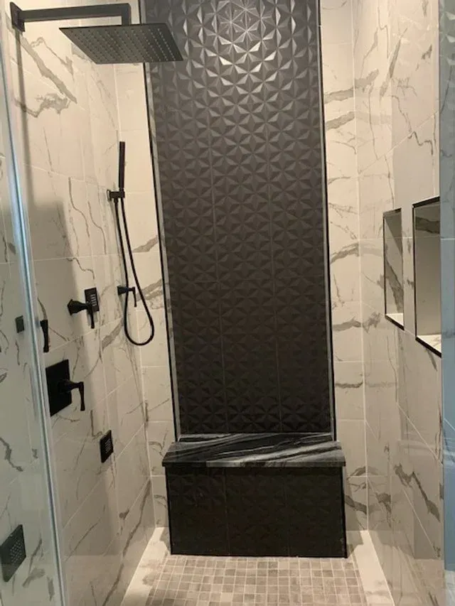 Modern shower with dark textured wall panel, handheld showerhead, and white marble-look tile walls.