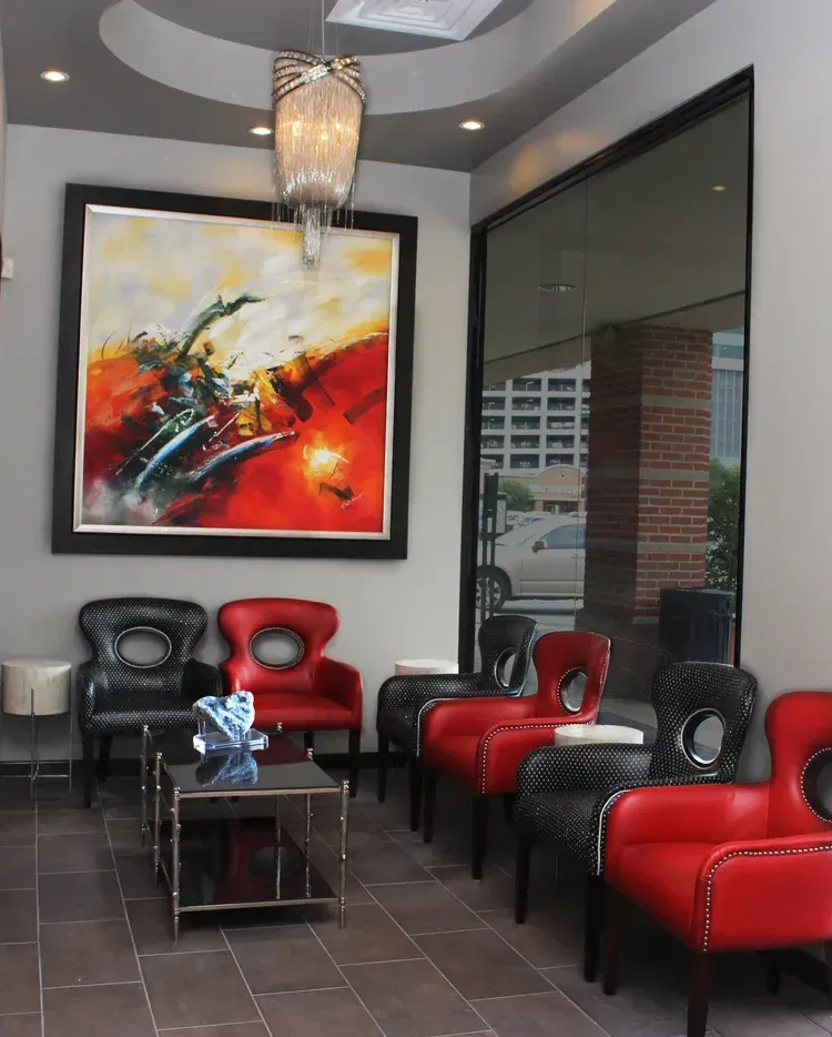 Modern lobby with black and red chairs, abstract wall art, glass table, and large window.