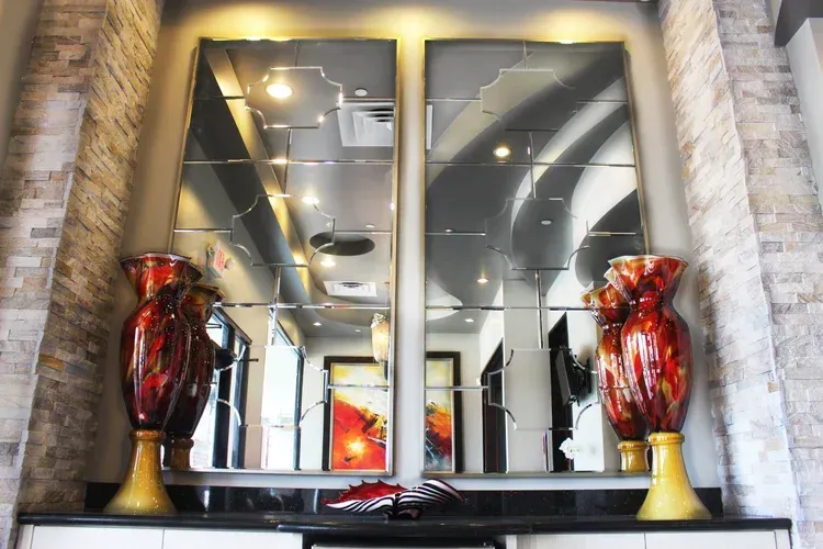 Modern interior with mirrored wall, two tall red vases, and stone columns surrounding a console table.