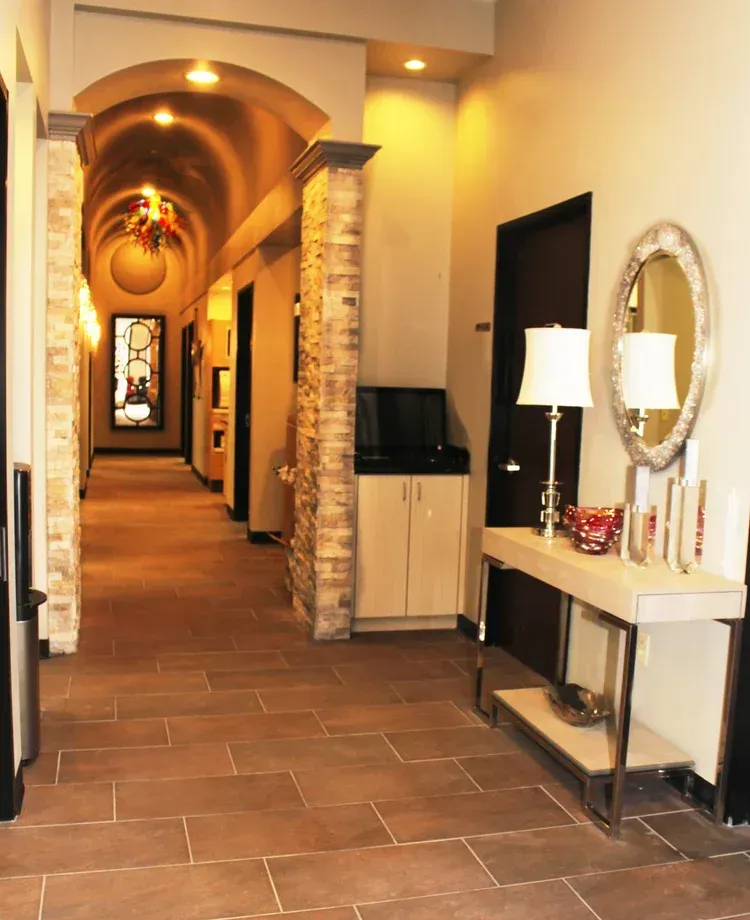 Elegant hotel hallway with arched ceiling, stone columns, tiled floor, and a console table with lamp and mirror