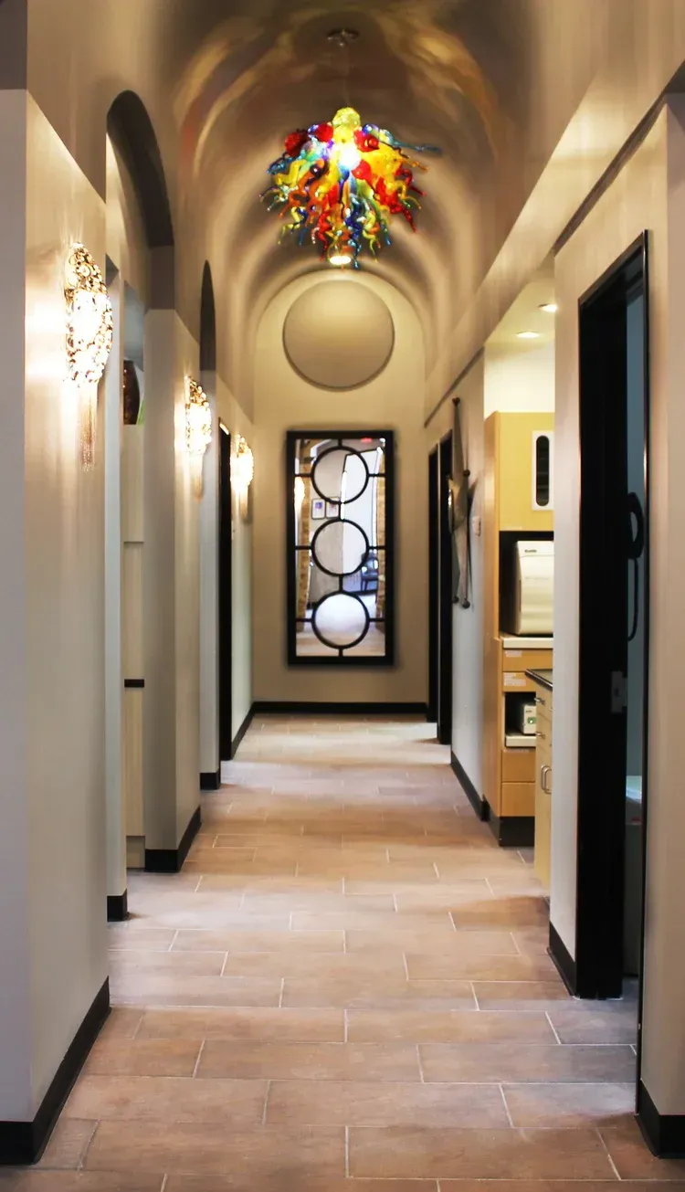 Narrow hallway with beige walls, arched ceiling, colorful chandelier, and a decorative glass door at the end