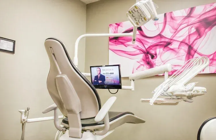 Dental exam chair with monitor and overhead light in a beige treatment room