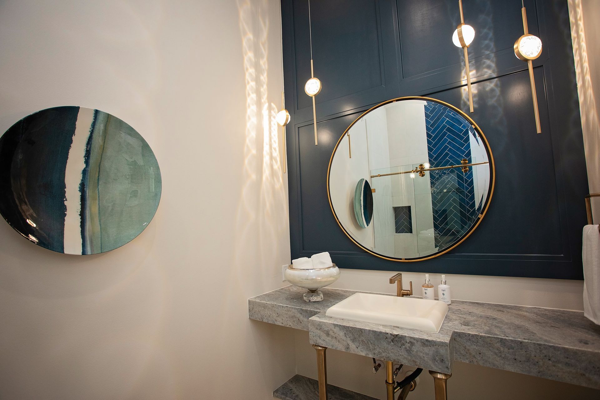 Modern bathroom vanity with round mirror, pendant lights, and blue-and-white wall decor