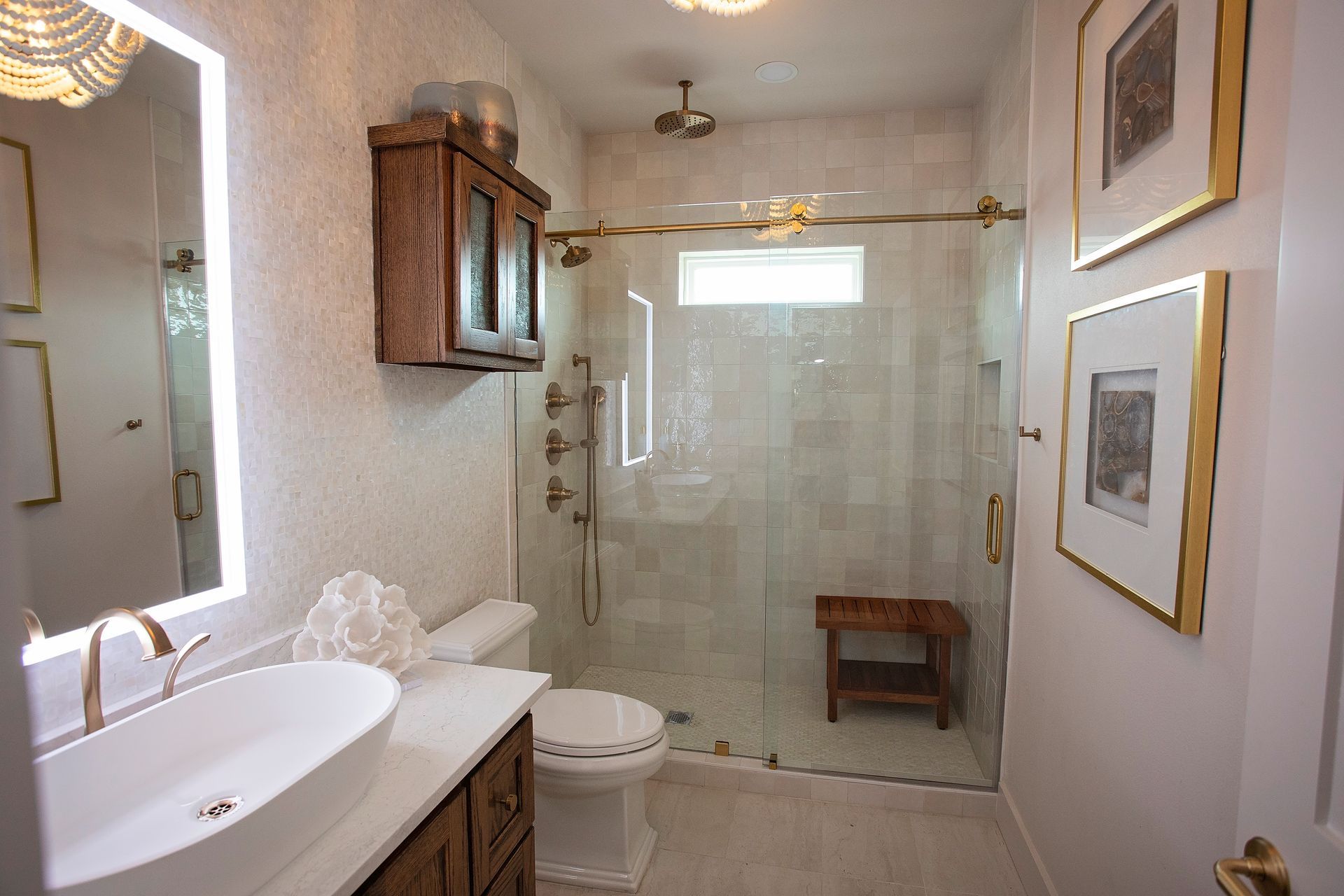 Bright white bathroom with vanity sink, toilet, shower, wood cabinet, and framed wall art.