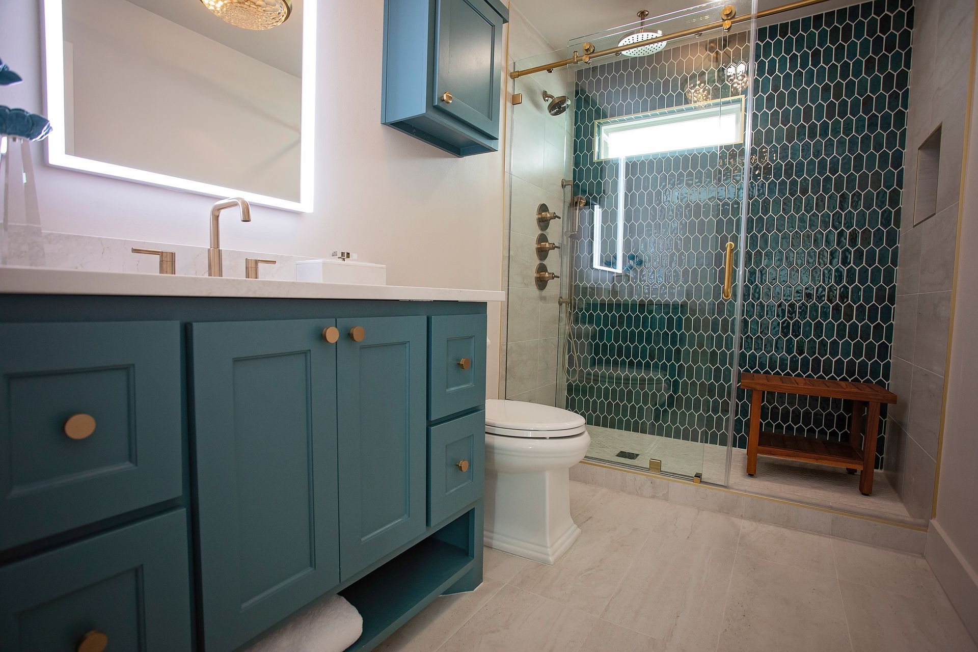Modern bathroom with teal vanity, mirror, toilet, and glass shower with dark tile.