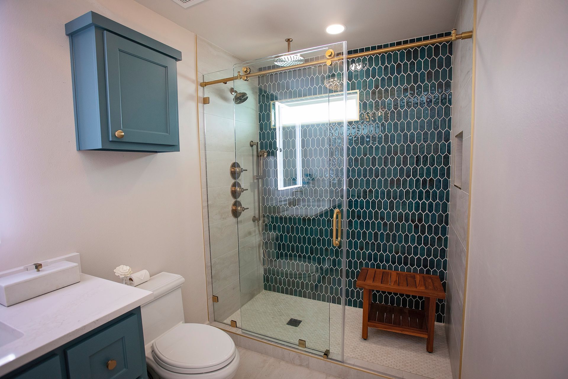Modern bathroom with glass shower, blue vanity, white toilet, and teal patterned shower curtain