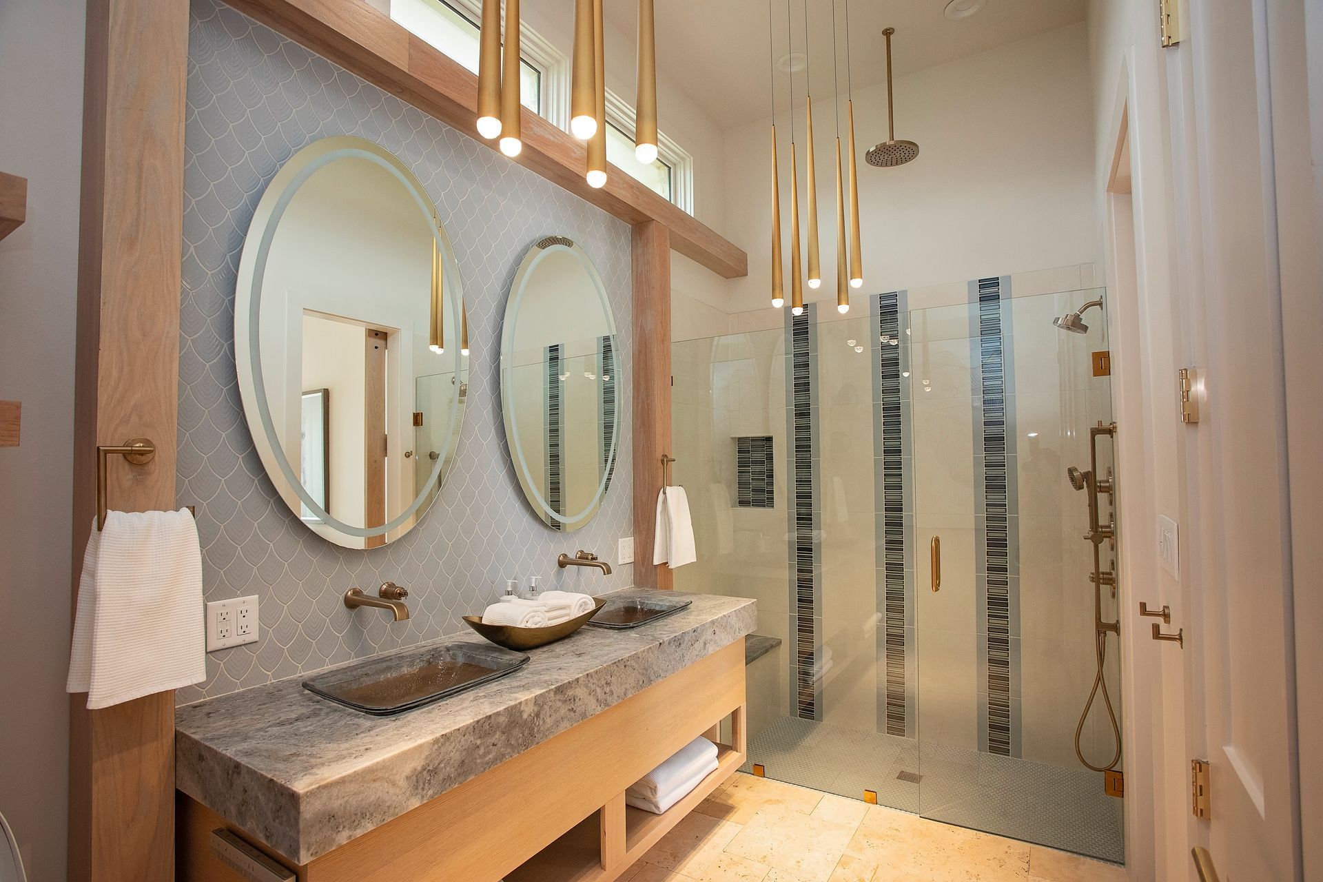 Modern bathroom with double oval mirrors, stone sink vanity, and glass shower with patterned panels.